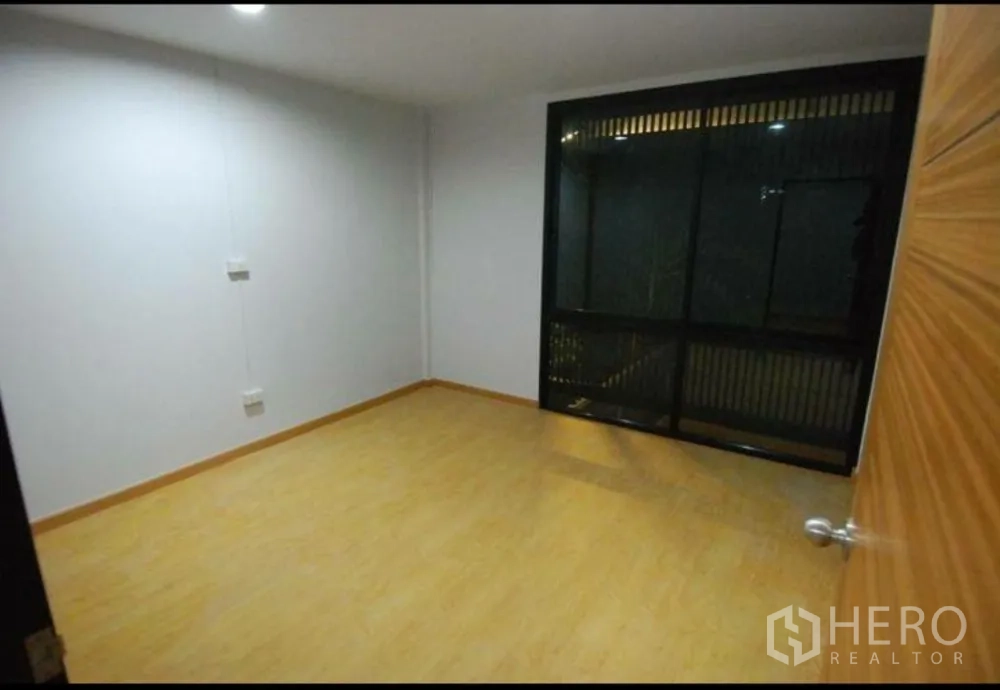 Home Office for rent in Lat Phrao, Bangkok - Cozy bedroom with wood flooring and dark-framed windows with privacy screens.