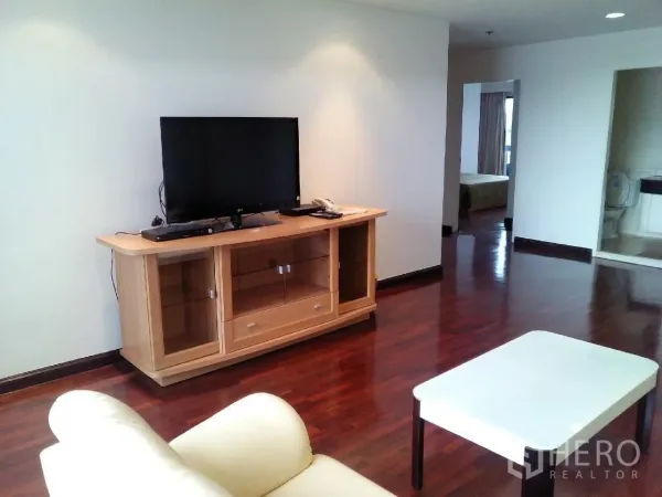 Condominium for rent in Phaya Thai, Bangkok - Bright living room with TV console, cream sofa, wooden floors and doorways to a bedroom and bathroom.