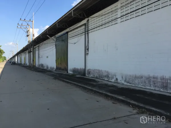 Factory for rent in Pathum Thani - Long row of white factory warehouses along a wide concrete road with power lines in Khlong Luang.