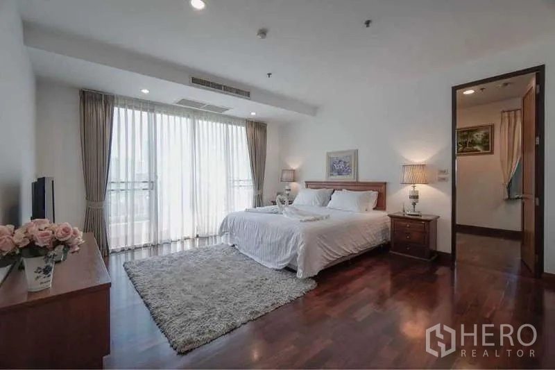 Apartment for rent in Sathon, Bangkok - Bright master bedroom with king bed, hardwood floors, bedside lamps and full-height windows with sheer curtains.