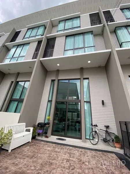 Townhouse for rent in Suan Luang, Bangkok - Contemporary three-storey townhouse exterior with tall glass entry and a paved courtyard.