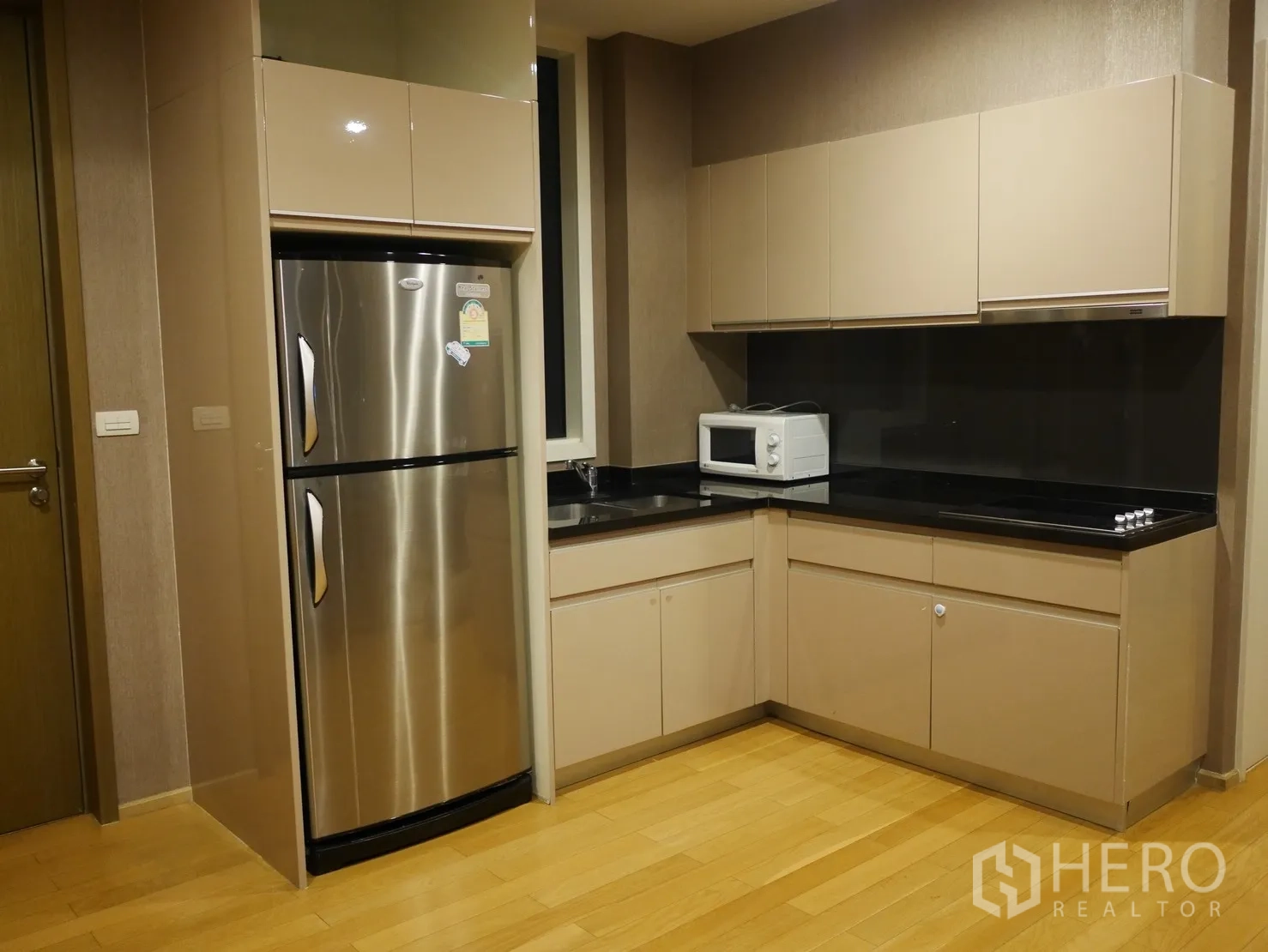 Condominium for rent in Watthana, Bangkok - Modern L-shaped kitchen with beige cabinetry, black countertop and stainless-steel fridge in a Bangkok condo.