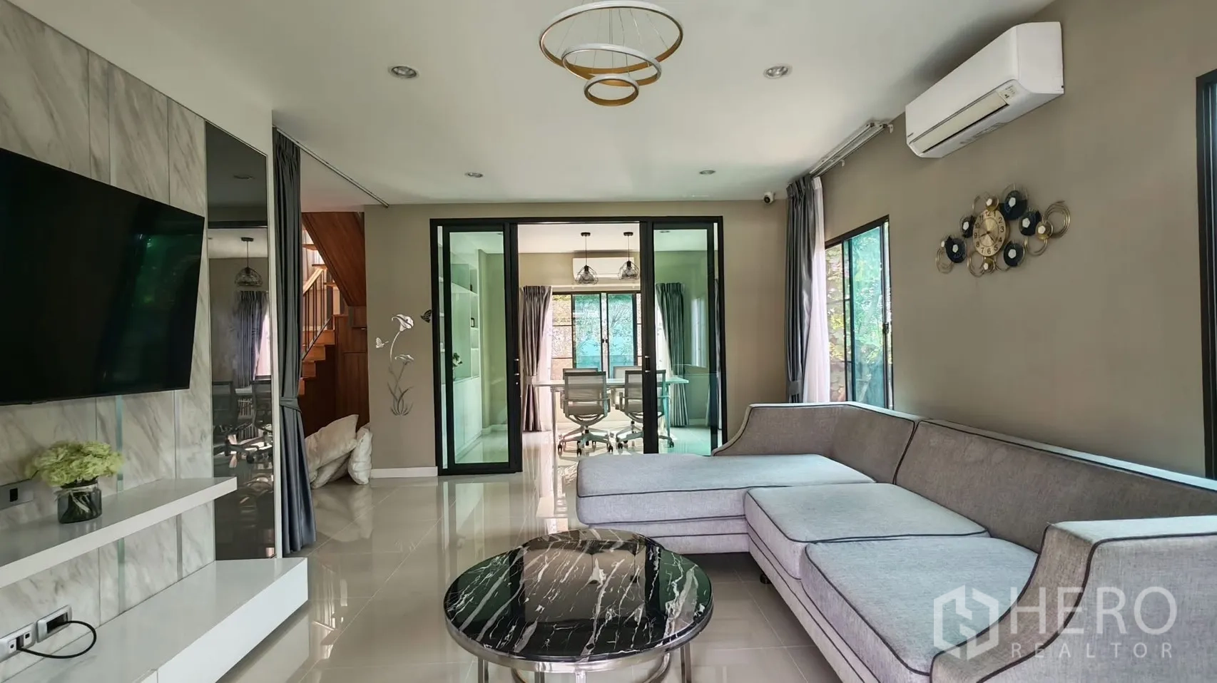 独栋房屋 for rent or sale in Bang Phli, Samut Prakan - 现代客厅，L形沙发、大理石背景墙，玻璃门通向书房。