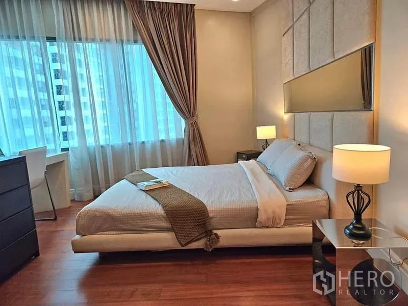 Condominium for rent or sale in Khlong Toei, Bangkok - Cozy bedroom with upholstered headboard, bedside lamps and a large curtained window.