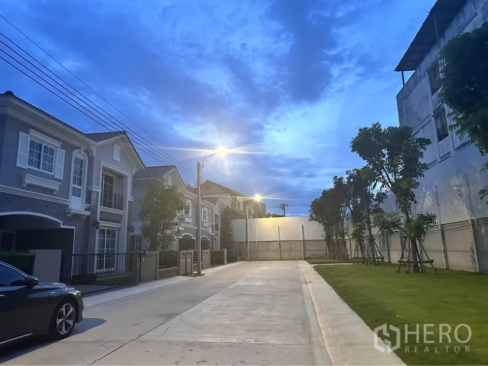 Semi-detached House for rent in Mueang Samut Prakan, Samut Prakan - Quiet residential street with similar houses, trees, and streetlights at dusk.