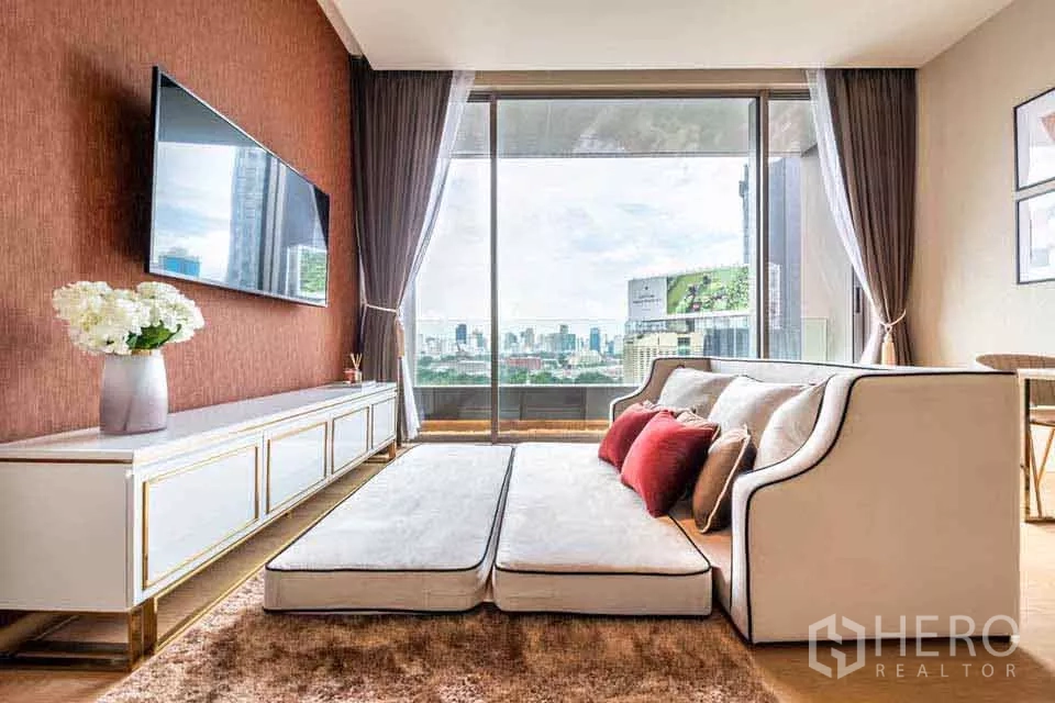 公寓 出租或出售在Bang Rak, Bangkok - 现代客厅，墙挂电视与沙发，推拉落地门外是城市天际线。