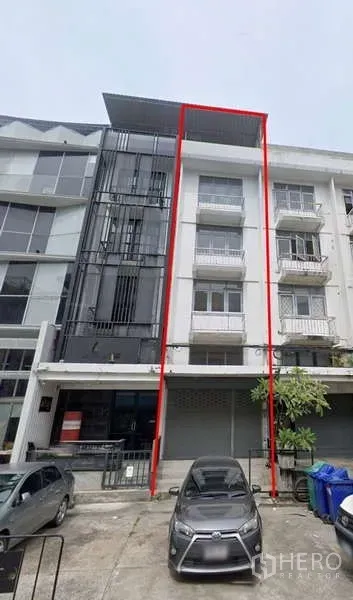 Shophouse for rent in Bang Na, Bangkok - Four-storey shophouse facade with balconies and a parking bay marked by red lines.