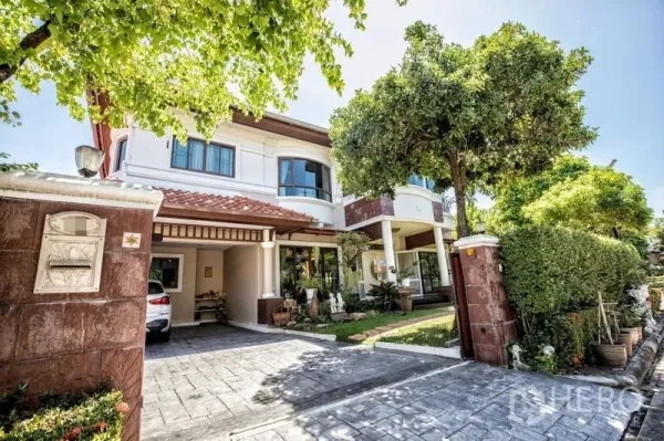 Detached House for sale in Lat Krabang, Bangkok - Two-storey detached house with tiled roof, gated driveway, carport and mature trees at the front.