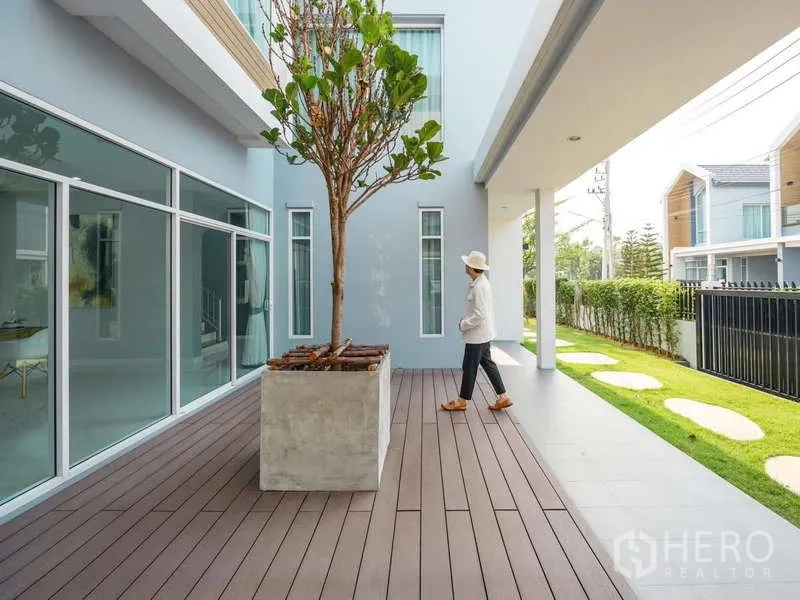 Detached House for sale in Lam Luk Ka, Pathum Thani - Private outdoor deck with planter tree beside glass walls and lawn.