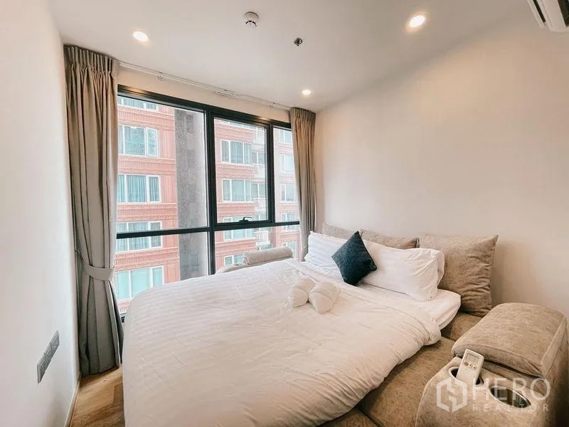 Condominium for rent in Ratchathewi, Bangkok - Second bedroom with bed, upholstered benches and wide window to nearby buildings.