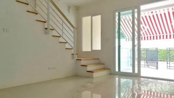 联排别墅 出租在Wang Thonglang, Bangkok - 采光充足的客厅，亮面地砖，白色扶手楼梯与通向庭院的推拉玻璃门