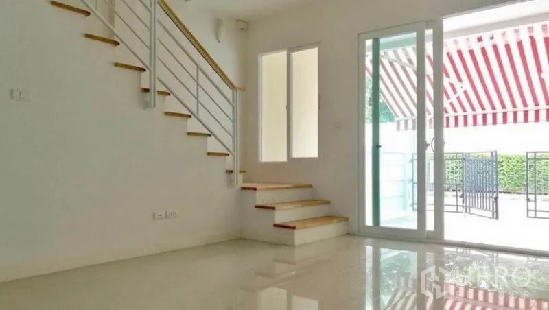 联排别墅 出租在Wang Thonglang, Bangkok - 采光充足的客厅，亮面地砖，白色扶手楼梯与通向庭院的推拉玻璃门