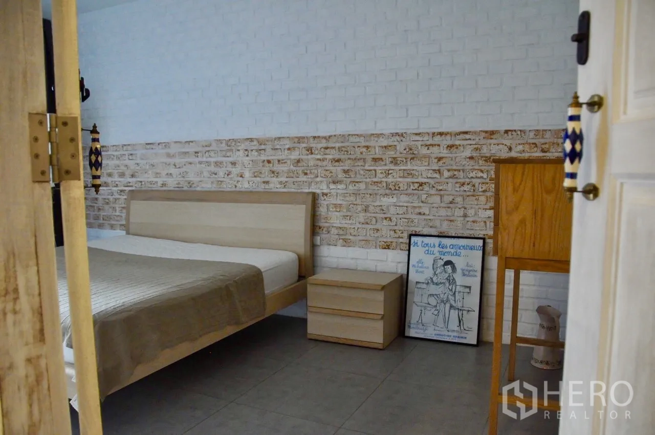 Condominium for rent in Bangkok - Cozy bedroom featuring a light wood bed, bedside table and a two-tone brick accent wall.