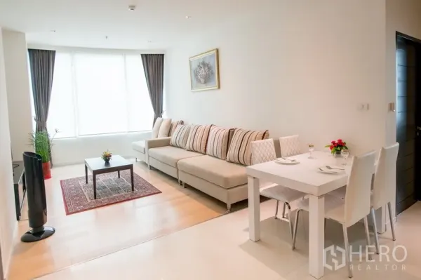 Condominium for rent in Watthana, Bangkok - Bright living and dining area with a large sectional sofa, white dining table, and floor-to-ceiling windows.