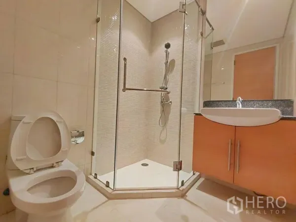 Condominium for rent in Watthana, Bangkok - Modern bathroom with glass-enclosed shower, vanity and toilet in neutral tiles.