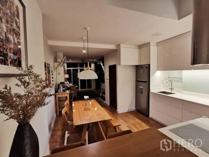 Townhouse for rent or sale in Yan Nawa, Bangkok - Dining area beside sleek white kitchen with wood table, pendant lights and ample cabinetry.