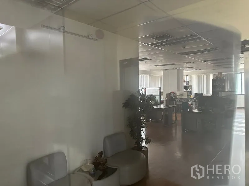 Office Space for rent in Bang Rak, Bangkok - Glass-partitioned view into an open-plan office featuring workstations, ceiling lighting, vertical blinds, and a compact waiting area.