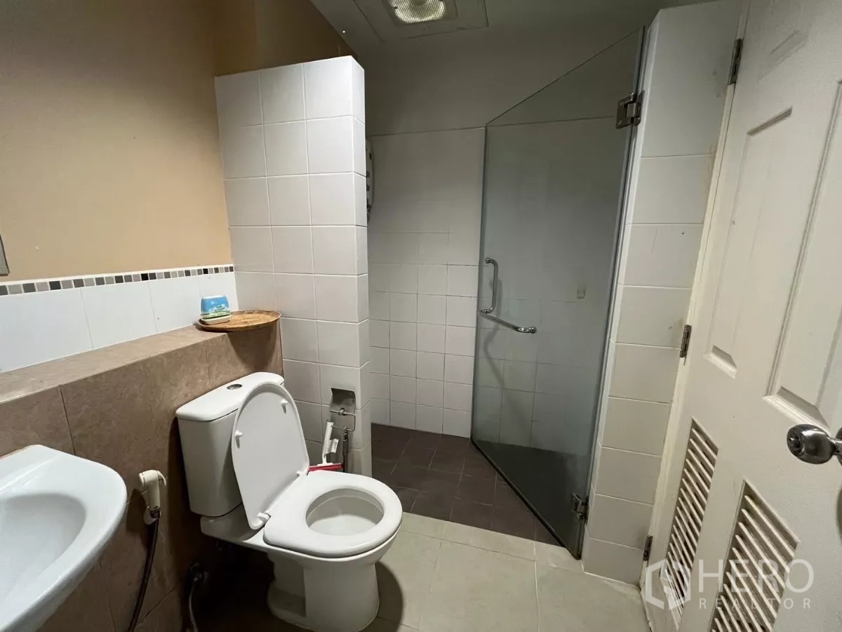 Townhouse for rent in Bang Kho Laem, Bangkok - Bathroom with glass-enclosed shower and toilet in neutral tiles.