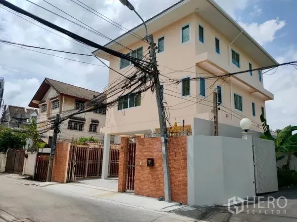 Detached House for rent in Khlong Toei, Bangkok - Street view of a multi-storey detached house with high brick fence and gated parking.