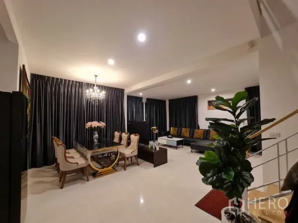 Detached House for rent or sale in Pathum Thani - Open-plan living and dining area with chandelier, marble table, leather seating, glossy tile floor and full-length curtains in a Thanyaburi detached house.