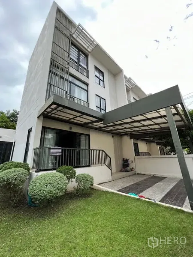 Townhouse for rent in Saphan Sung, Bangkok - Modern three-storey townhouse exterior with carport, lawn, and trimmed shrubs.