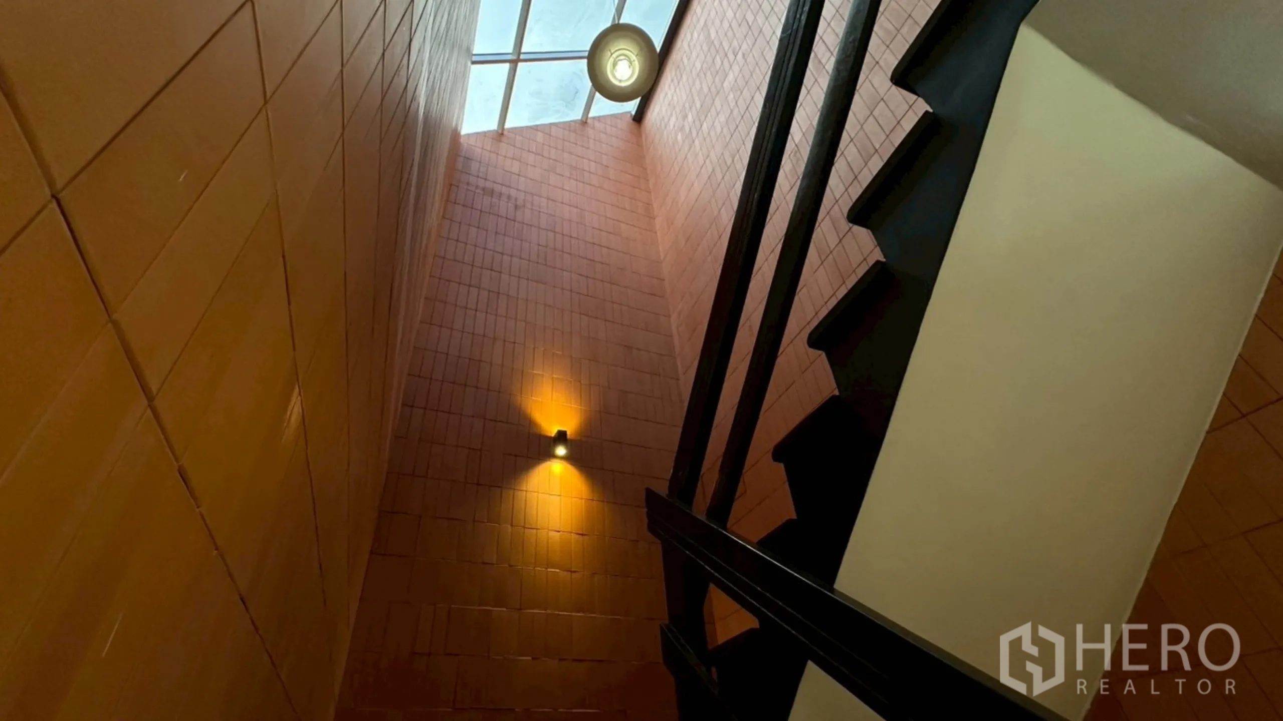 Home Office for rent in Watthana, Bangkok - Stairwell beneath skylight with uplights on terracotta walls and black stairs.