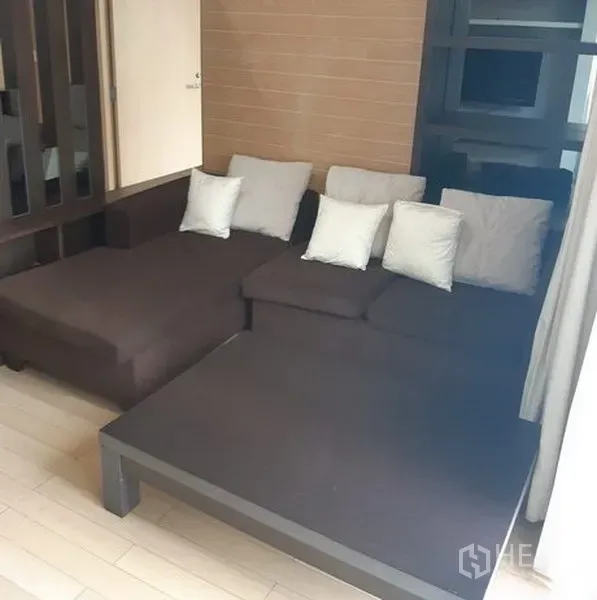 公寓 出租在Khlong Toei, Bangkok - 客厅配深色L型沙发与原木色地板。