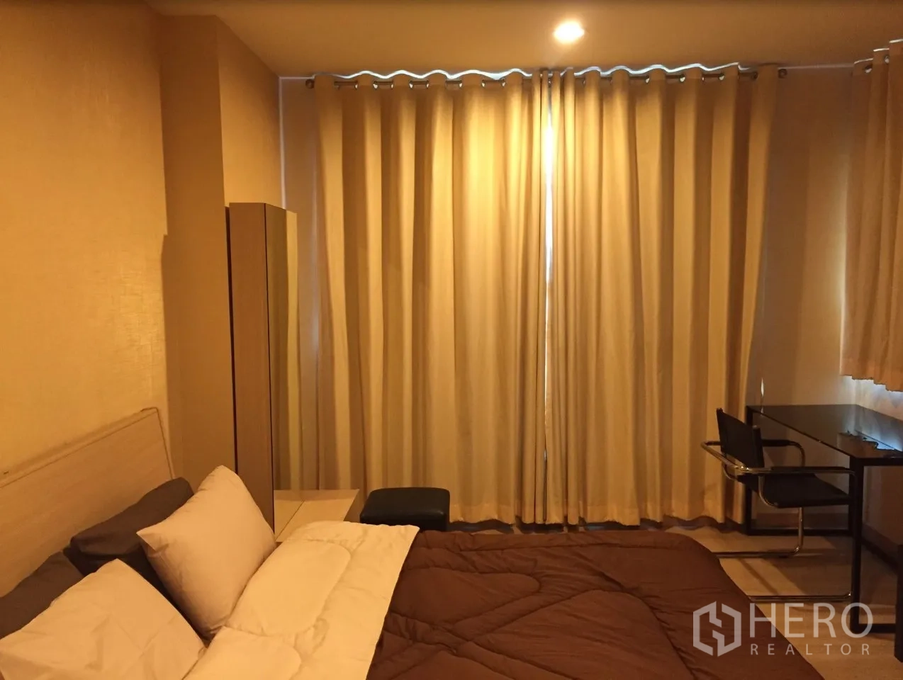 Condominium for rent in Bang Rak, Bangkok - Warm-toned bedroom with double bed, blackout curtains and a work desk.