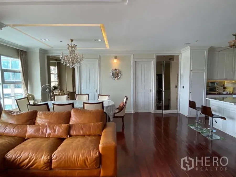 Condominium for rent in Ratchathewi, Bangkok - Open-plan living and dining area with leather sofa, chandelier, and polished wood floors in a Ratchathewi condo.