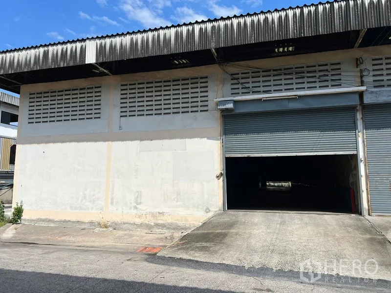 Warehouse for rent in Mueang Samut Prakan, Samut Prakan - Warehouse exterior with roller shutter loading bay, drive-up ramp, ventilation blocks, and corrugated roof.