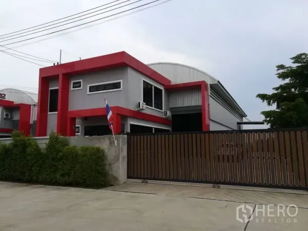 โรงงาน for sale in Bang Len, Nakhon Pathom - อาคารโรงงานสมัยใหม่พร้อมออฟฟิศ 2 ชั้น โทนแดงเทาและประตูรั้วหน้าโครงการ