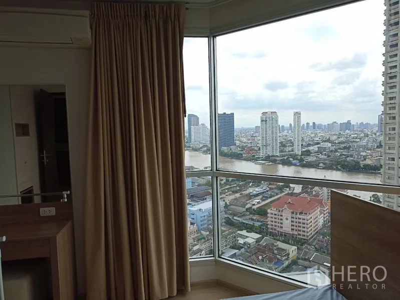 公寓 出租或出售在Sathon, Bangkok - 卧室转角落地窗，框出河景与天际线，配米色窗帘。