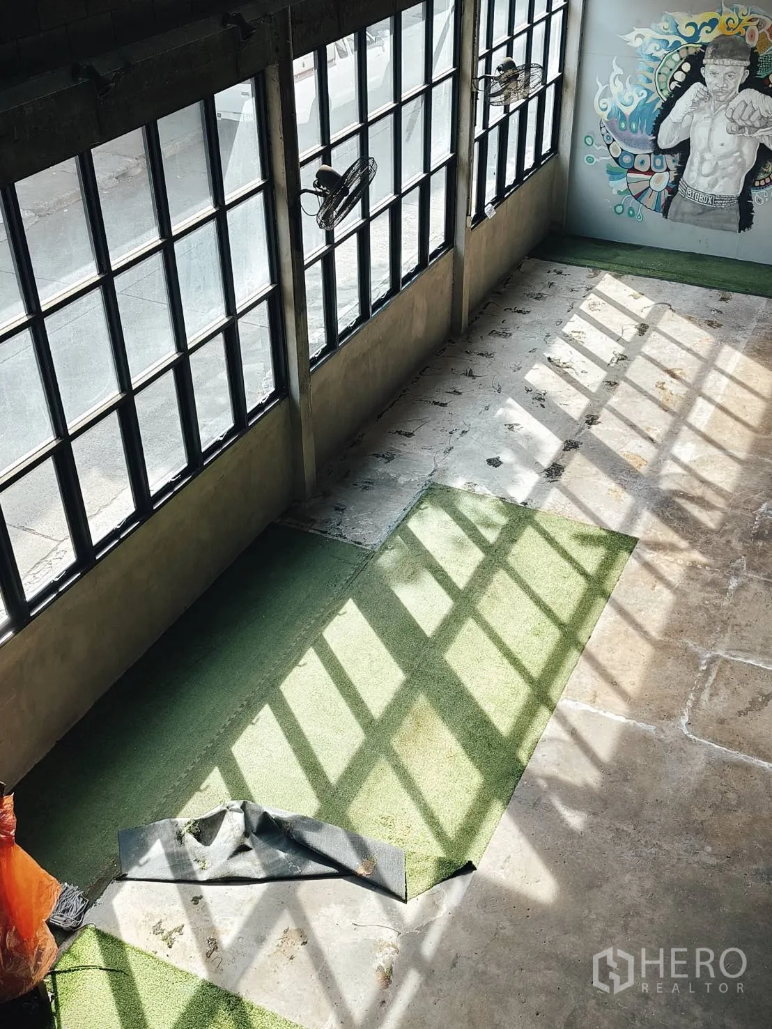 货栈 出租在Khlong Toei, Bangkok - 采光充足的仓库内部，格栅大窗、混凝土地面、人工草带与彩色墙面涂鸦。