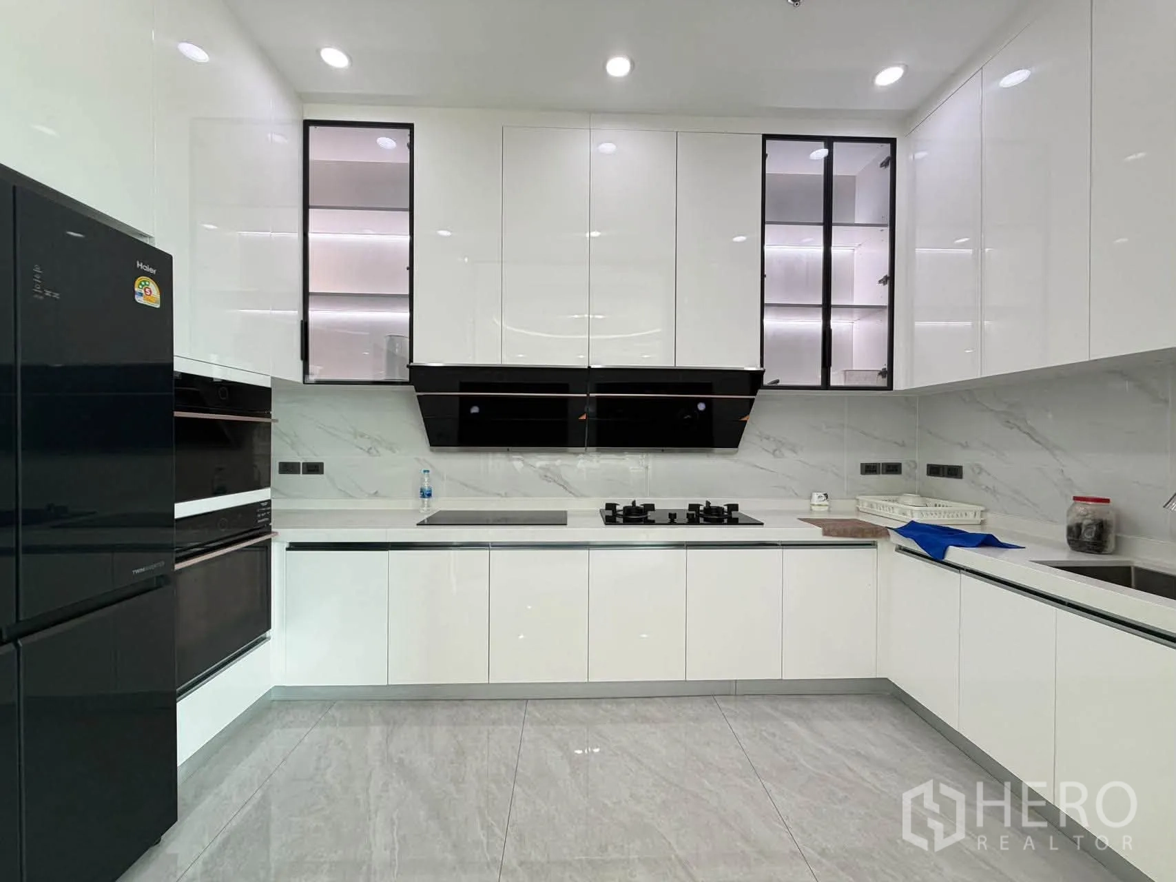 Condominium for sale in Watthana, Bangkok - Sleek white U-shaped kitchen with gas hob, hood, and glossy cabinets.