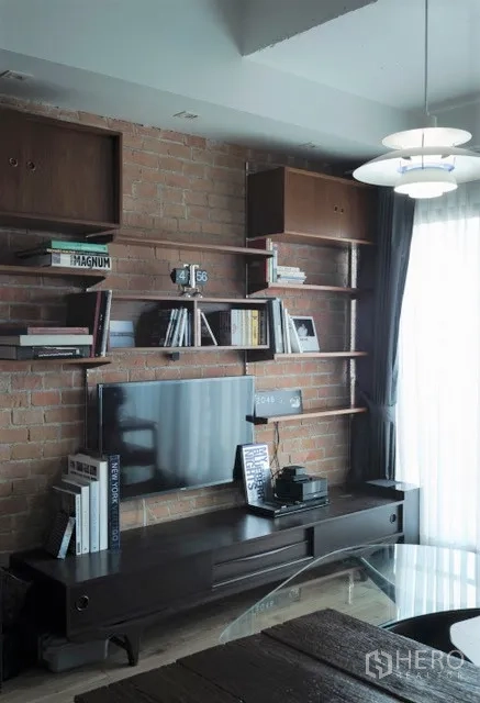 Condominium for rent in Khlong Toei, Bangkok - Exposed-brick feature wall with TV console and open shelves filled with books.