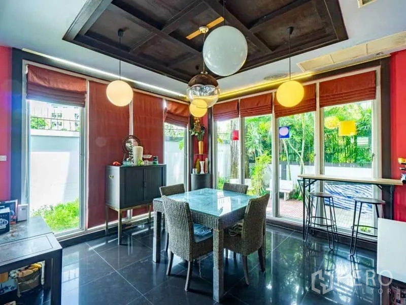 独立式住宅 出售在Suan Luang, Bangkok - 明亮餐厅，玻璃餐桌、圆形吊灯与花园景观。