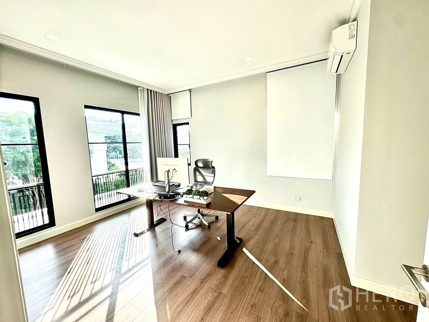 Detached House for rent in Bang Phli, Samut Prakan - Sunlit home office with corner windows, balcony view and a modern desk on warm wood floors.