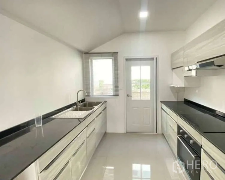 Detached House for sale in Bang Khen, Bangkok - Fitted Western kitchen with twin counters, sink, cooktop, range hood, window and door to the yard.