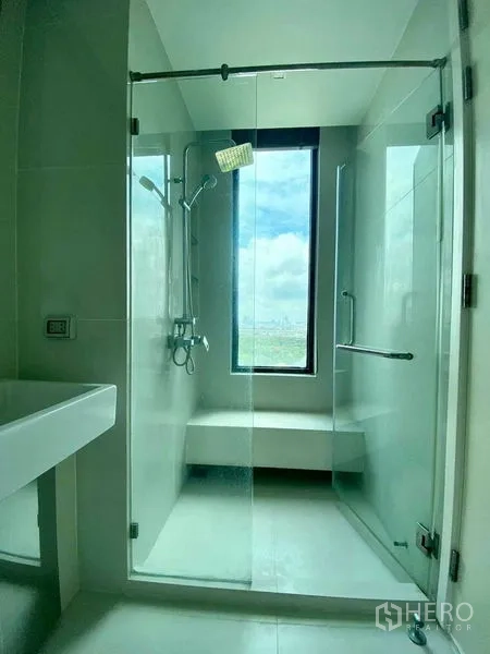 Condominium for rent in Bangkok - Bathroom with glass-enclosed shower, window and rainfall shower head.