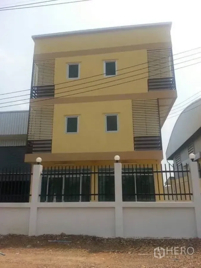 Factory for rent or sale in Khlong Luang, Pathum Thani - Three-storey yellow office building with louvered balconies and a front fence at a factory site in Khlong Luang.