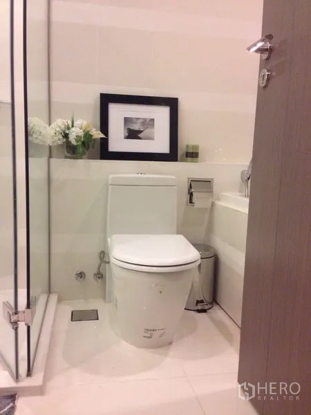 Condominium for rent in Khlong Toei, Bangkok - Modern bathroom with glass shower enclosure, white toilet and vanity.