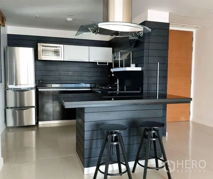 Condominium for rent in Watthana, Bangkok - Modern black kitchen with island, bar stools, and stainless steel appliances.