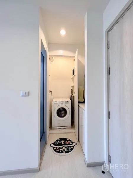 Condominium for rent or sale in Khlong Toei, Bangkok - Laundry nook with front-loading washing machine and shelving in a small corridor.