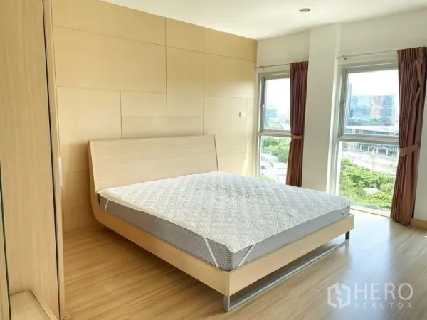 Condominium for rent in Khlong Toei, Bangkok - Sunlit bedroom with light wood panel wall, bed frame and corner windows overlooking the city.