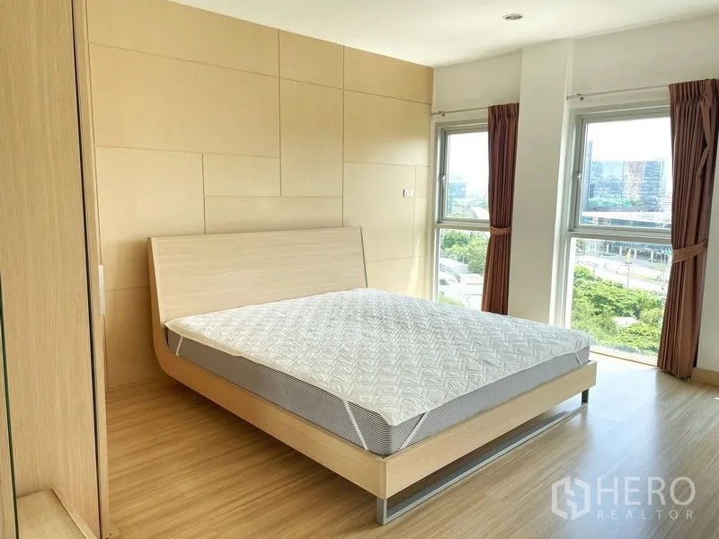 Condominium for rent in Khlong Toei, Bangkok - Sunlit bedroom with light wood panel wall, bed frame and corner windows overlooking the city.