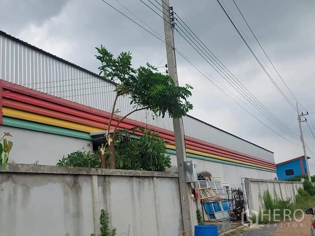 仓库 for sale in Lam Luk Ka, Pathum Thani - 仓库侧立面，混凝土围墙内设通风百叶与架空电线。