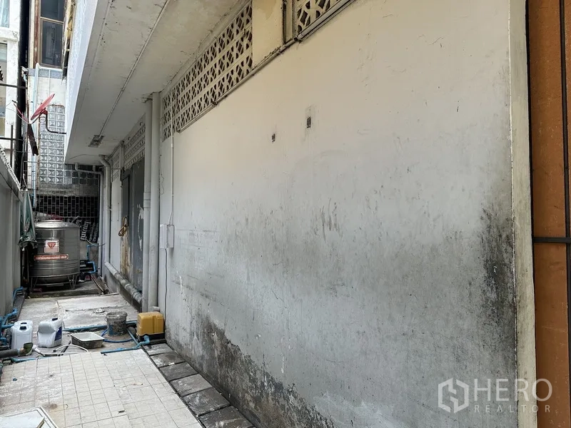 Retail Space for rent in Bang Rak, Bangkok - Narrow service alley with tiled floor, exposed pipes, and a stainless water tank beside the building.