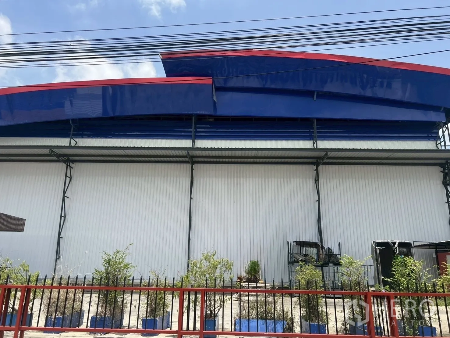 货栈 出租在Lat Krabang, Bangkok - 叻甲挽仓库正立面，蓝红色檐口、白色金属墙板与围栏绿化带。