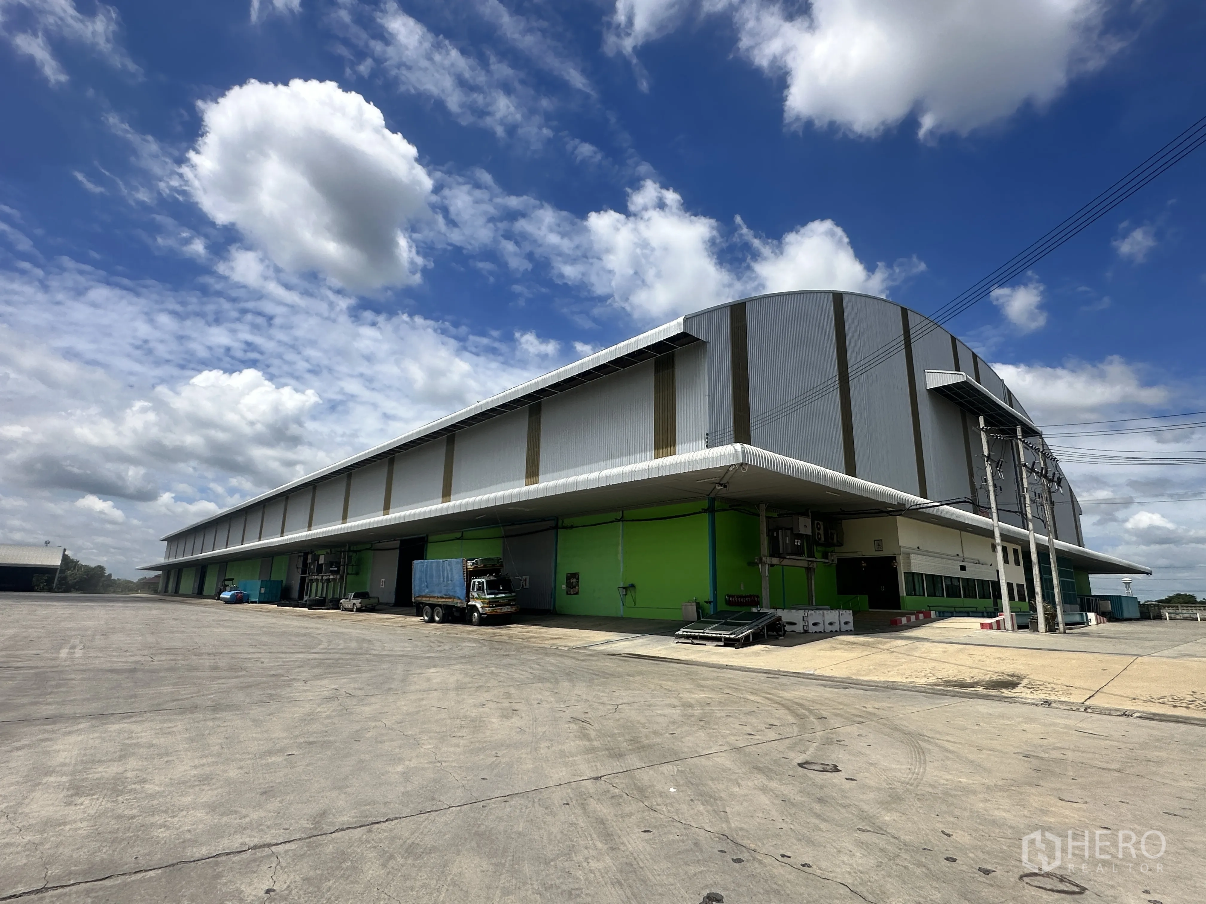 Warehouse for rent in Sai Noi, Nonthaburi - Angled exterior view of the large warehouse building with extensive yard space for truck maneuvering.