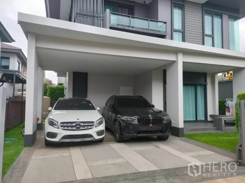 Detached House for rent or sale in Lam Luk Ka, Pathum Thani - Contemporary two‑storey house facade with balcony and a covered carport for two cars.